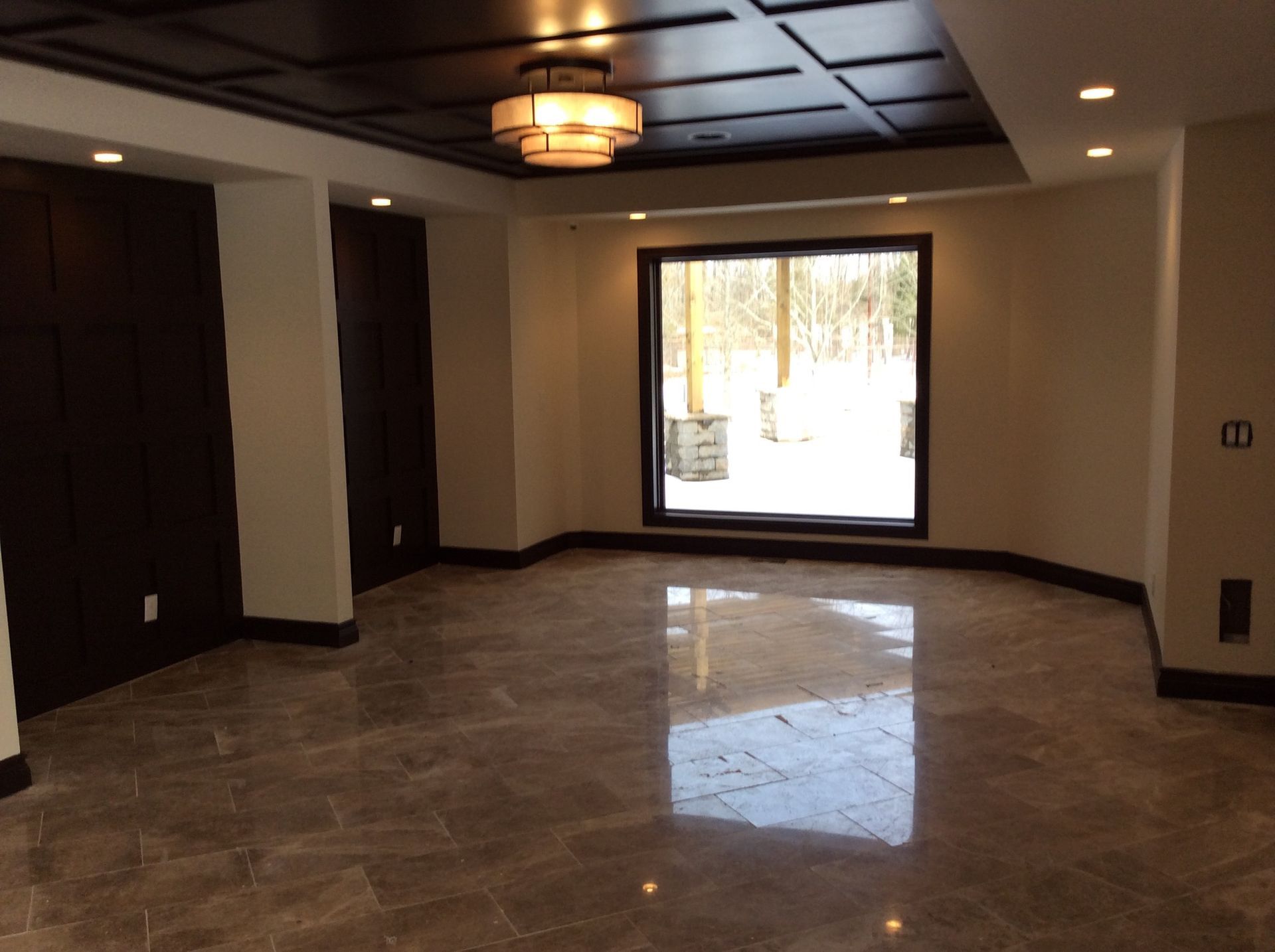 Dining room with a dark coffered ceiling, a drum light fixture, a large picture window and the same polished stone floor.