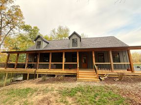 House exterior: a story-and-a-half house with two front dormers in board-and-batten siding, a long front porch on cedar posts with a black-baluster railing, and wide cedar steps.