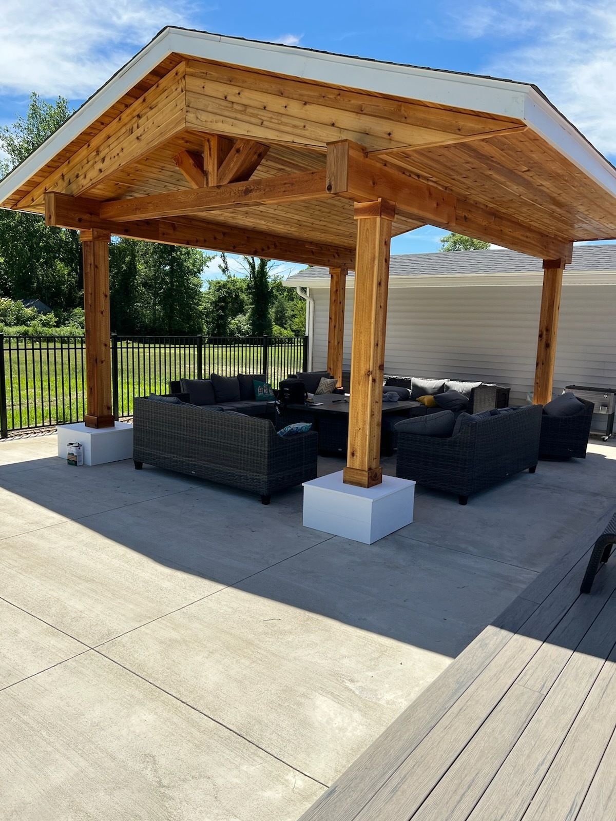 Backyard pavilion: a freestanding cedar pavilion with a king-post truss and a tongue-and-groove ceiling over an outdoor sectional, on a concrete patio beside a deck.
