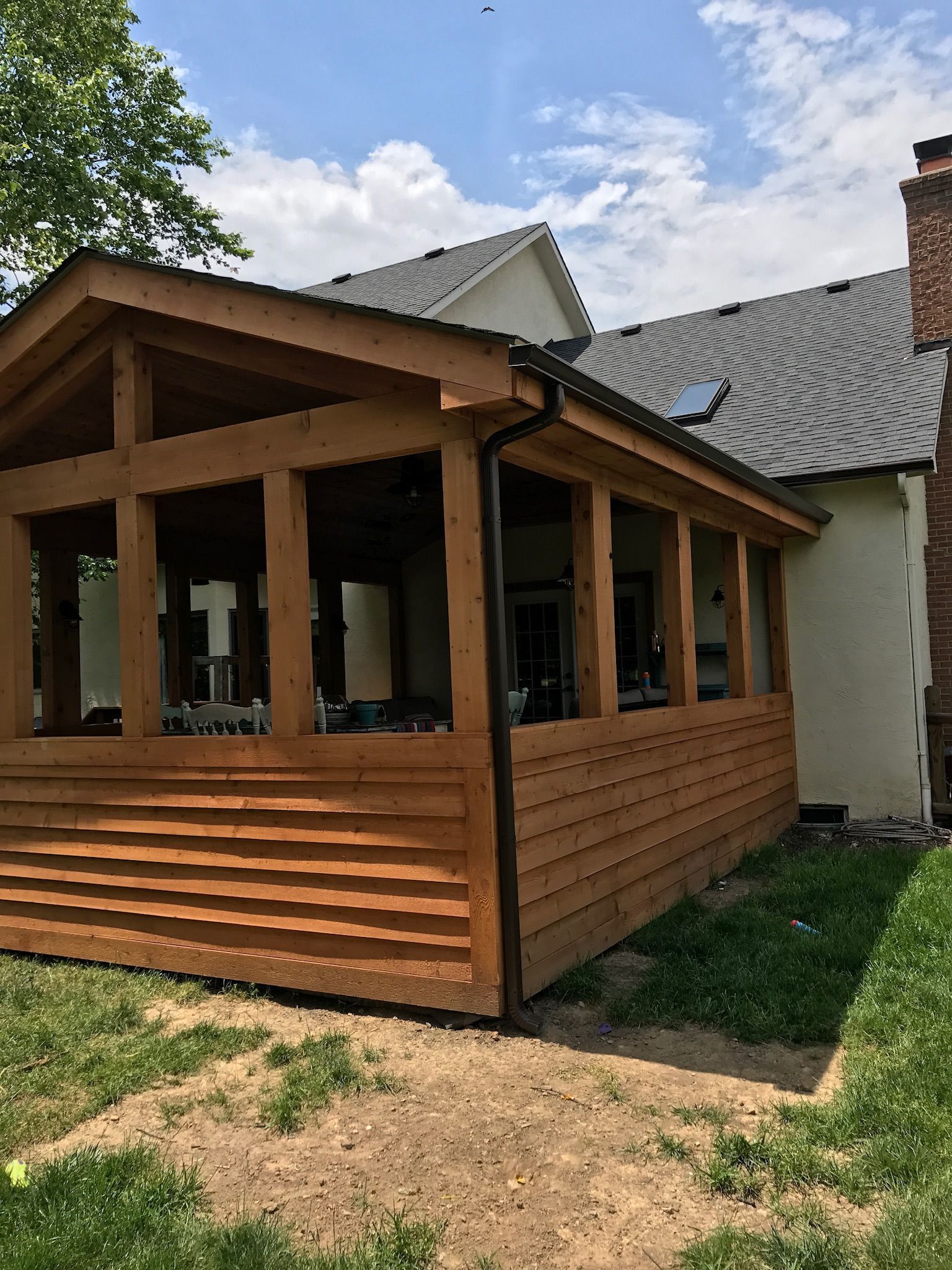 Screened porch on the back of a house: cedar posts and horizontal cedar boards under a gable roof, with screened openings above the knee wall.