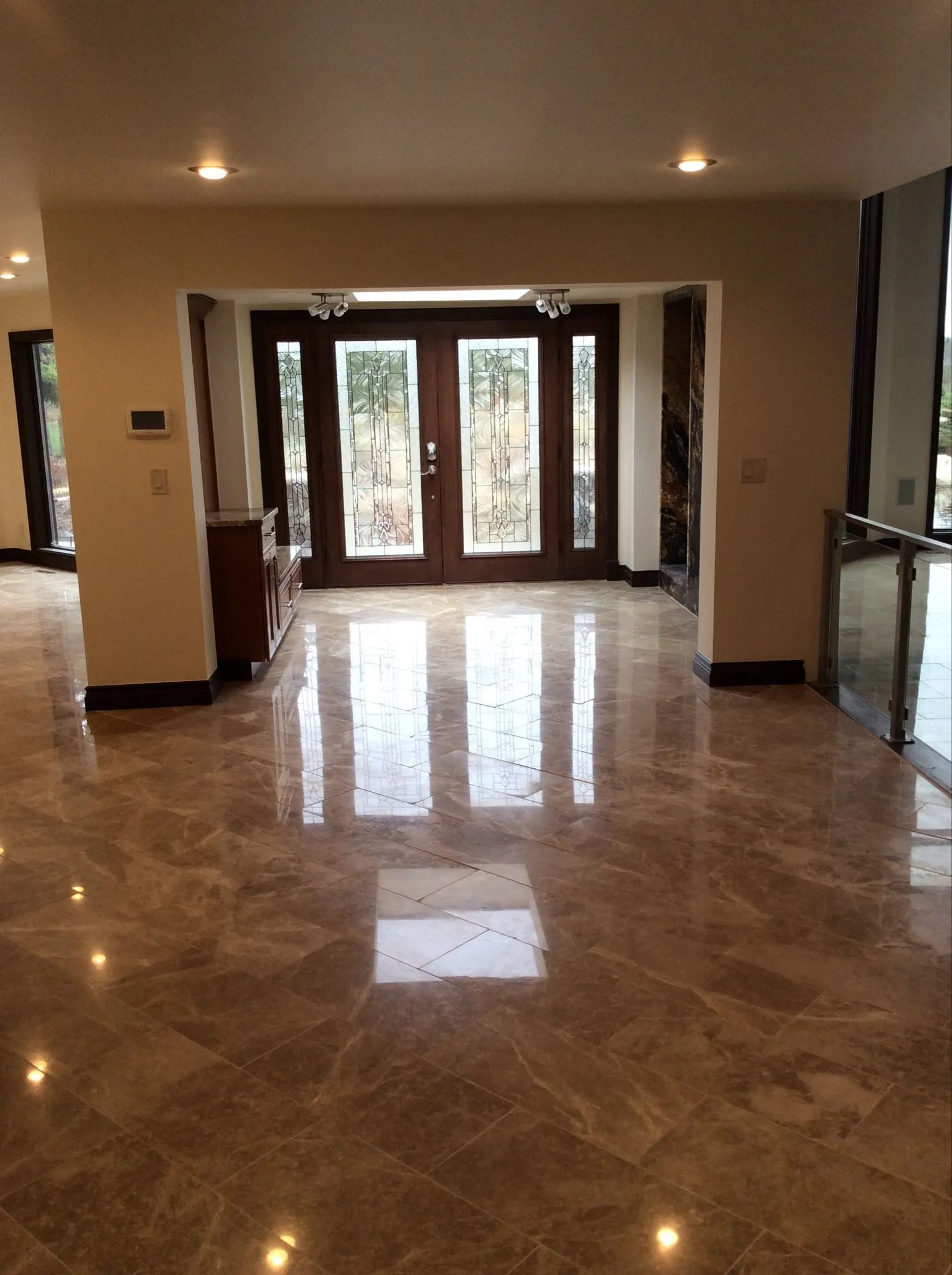 Entry: double doors with leaded glass and matching sidelights at the end of a polished stone floor, with a glass railing at right.