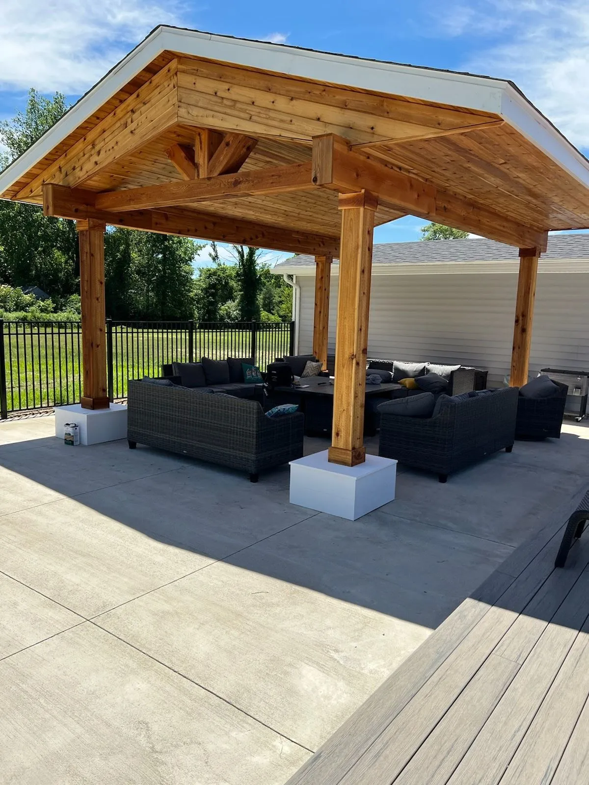 Backyard pavilion: a freestanding cedar pavilion with a king-post truss and a tongue-and-groove ceiling over an outdoor sectional, on a concrete patio beside a deck.