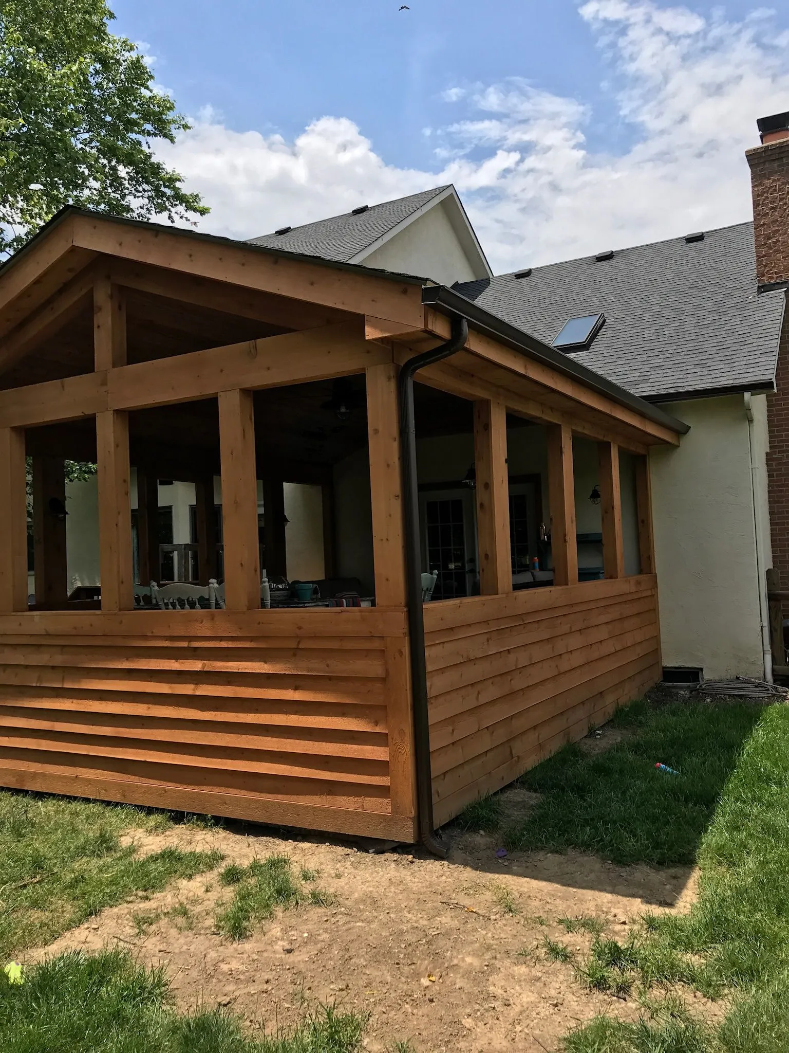 Screened porch on the back of a house: cedar posts and horizontal cedar boards under a gable roof, with screened openings above the knee wall.