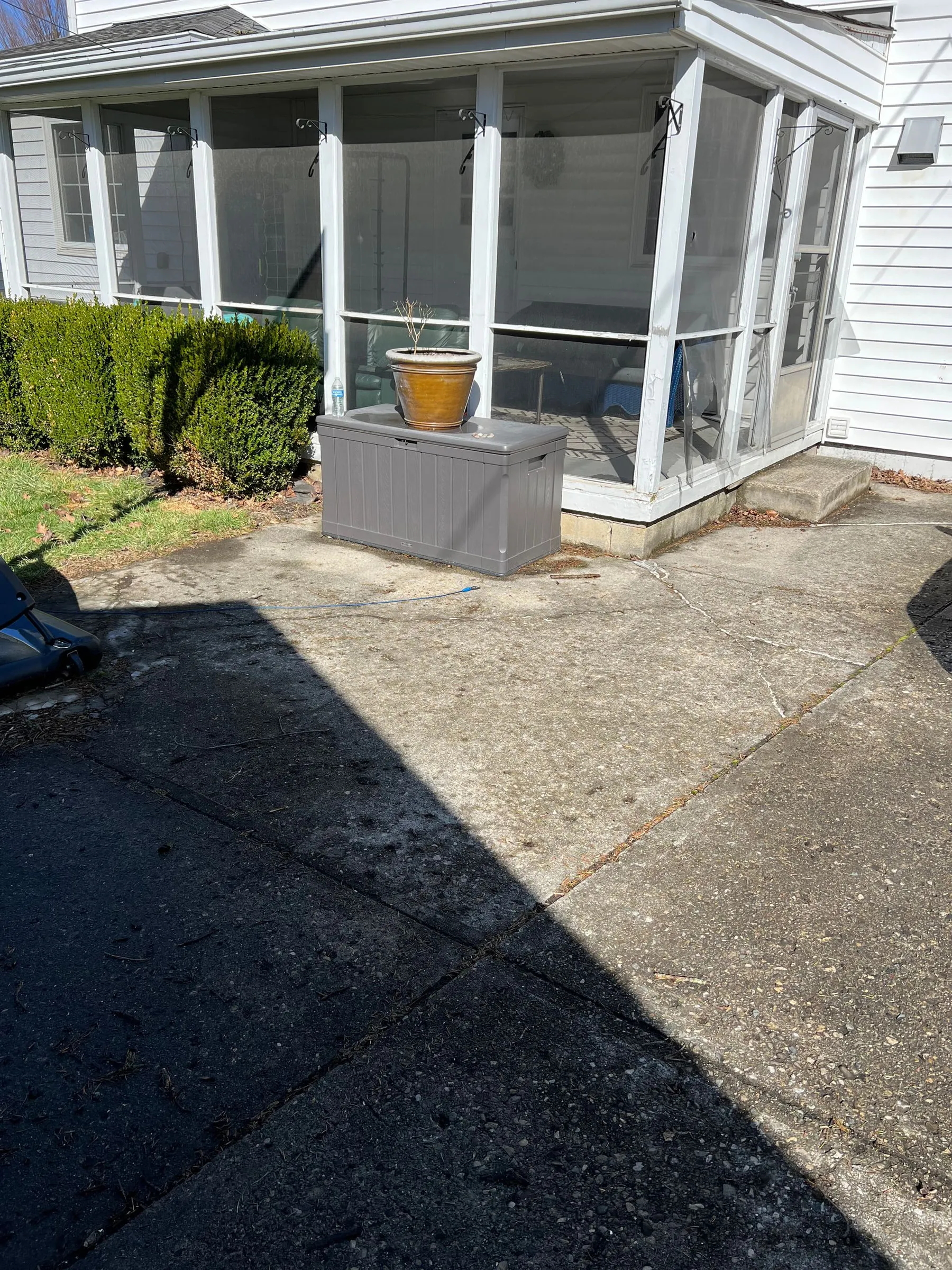Front porch on a two-story white-sided house, enclosed with screen panels between square white posts, with a step at the door and a concrete drive in front.